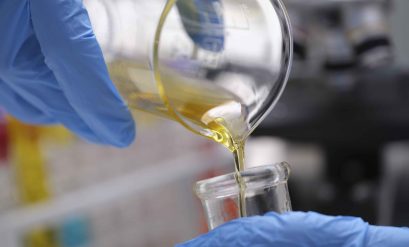 Chemical laboratory research and liquid oil processing. Scientist manually pouring yellow liquid from a chemical test tube into a glass flask concept